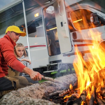 A father and daughter tending the fire outside a Class C RV.