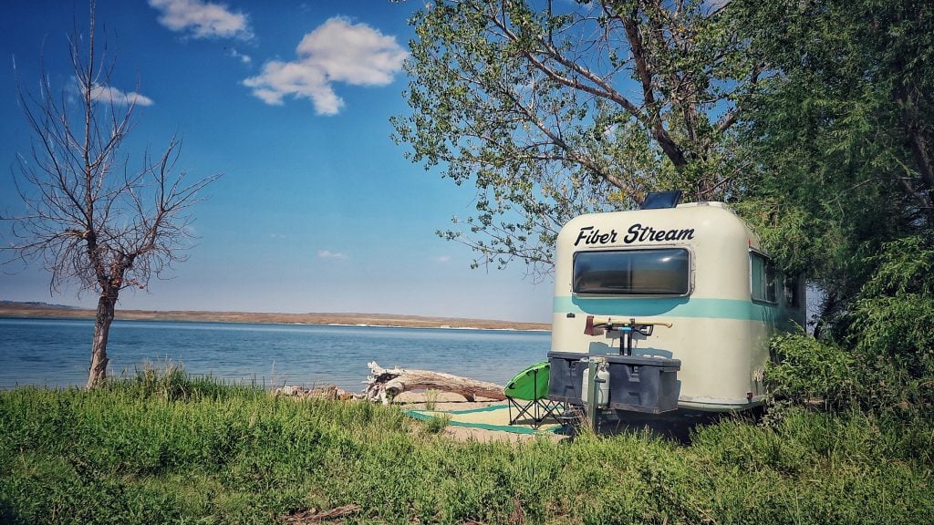 A towable RV nestled in the trees and a large blue river in the background. 