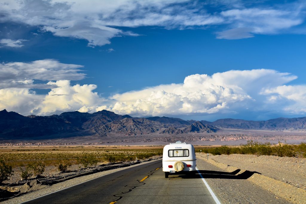 Small camper trailer being towed down the open road with mountains in the background