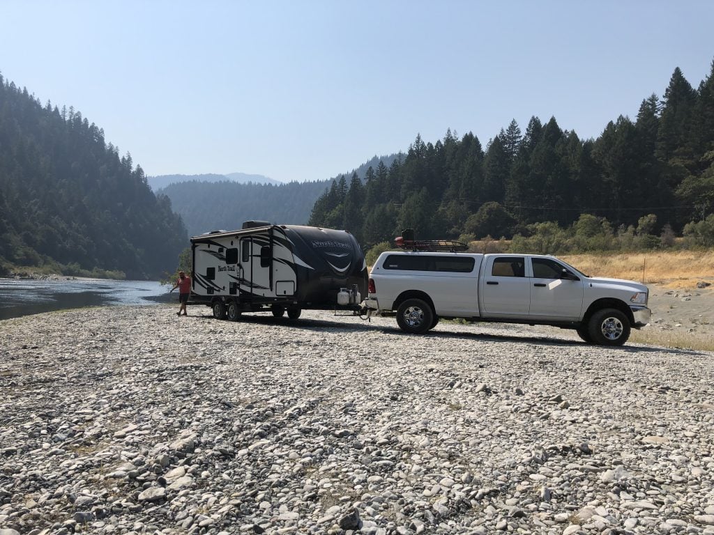 Truck with a small camper trailer boondocking on a river bed