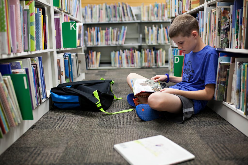 boy learning how to homeschool sitting in the library with books