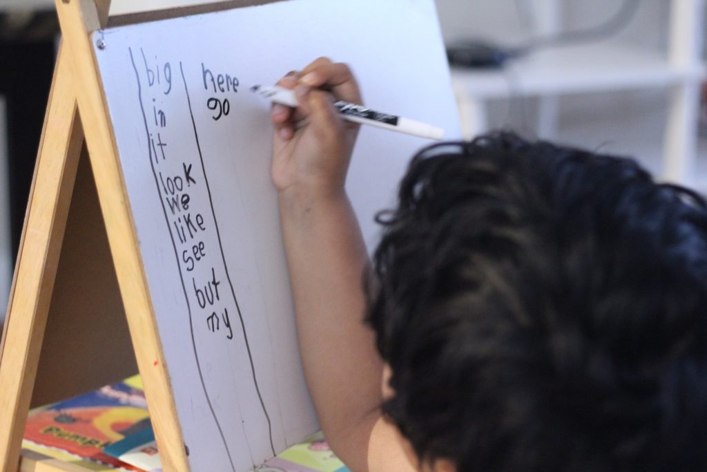 Boy with black hair in his favorite roadschool groups using an easel and paper to write words 