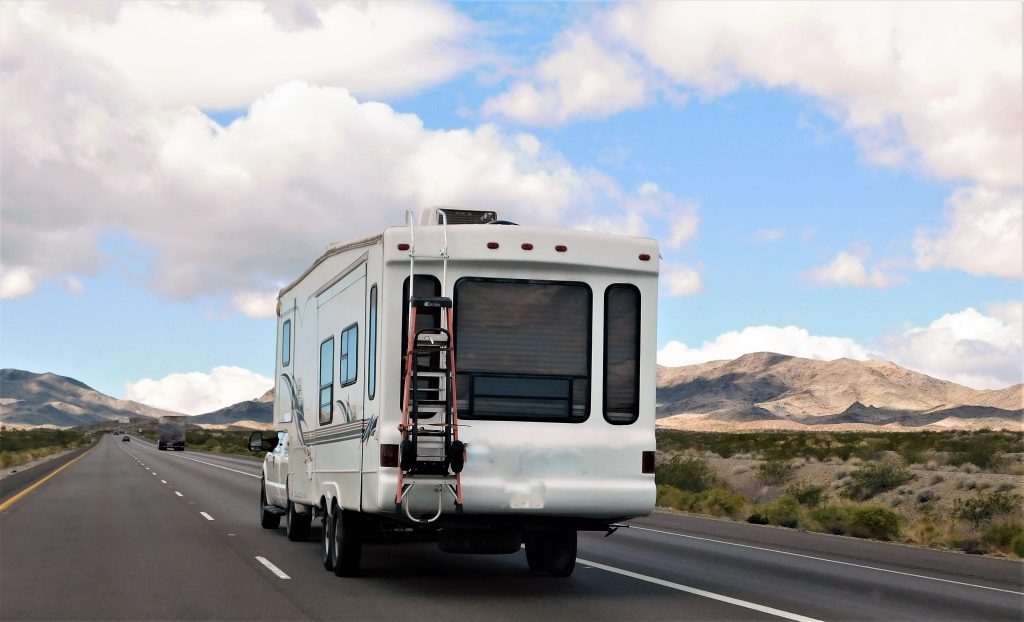 A fifth wheel driving down the highway with clouds in the sky, on of the largest types of towable RVs on the market.