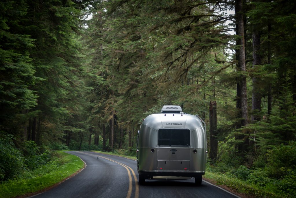 An airstream RV being towed down the highway with trees and green grass. When RV towing, make sure your weight is evenly distributed.
