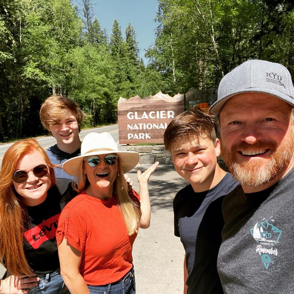 Popular RV bloggers, The KYD family standing in front of the Glacier National Park entrance sign