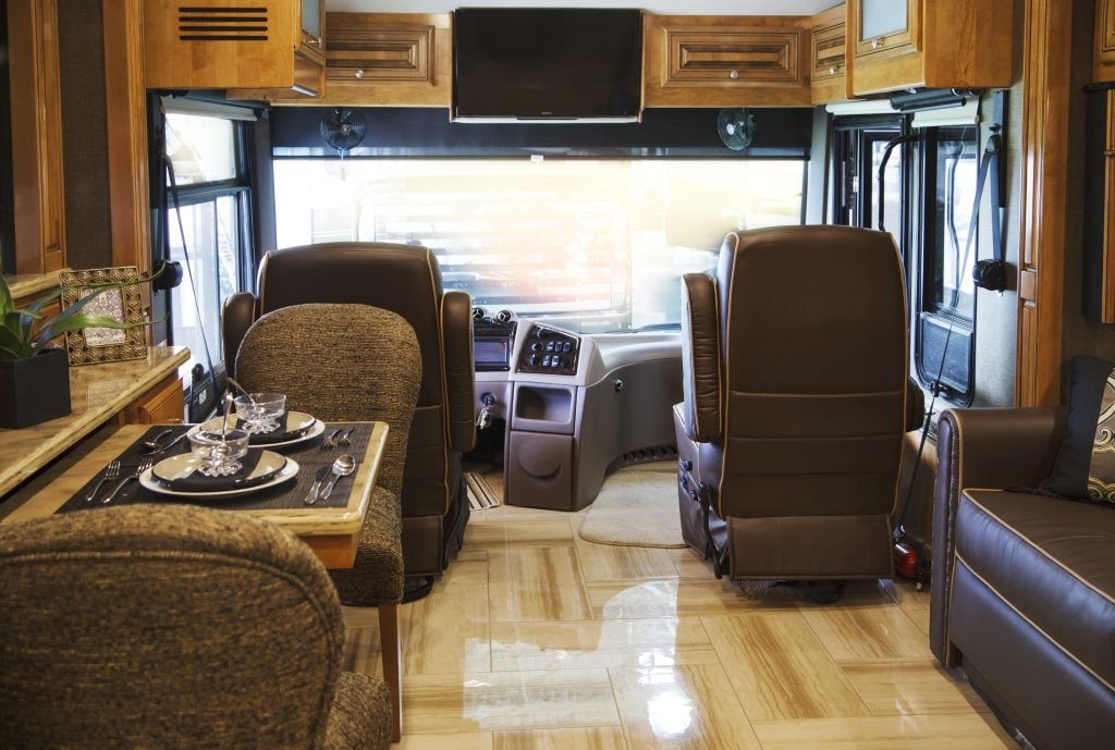 Interior shot of a class A RV showing the dining table setup and the cockpit chairs facing the large windshield. 