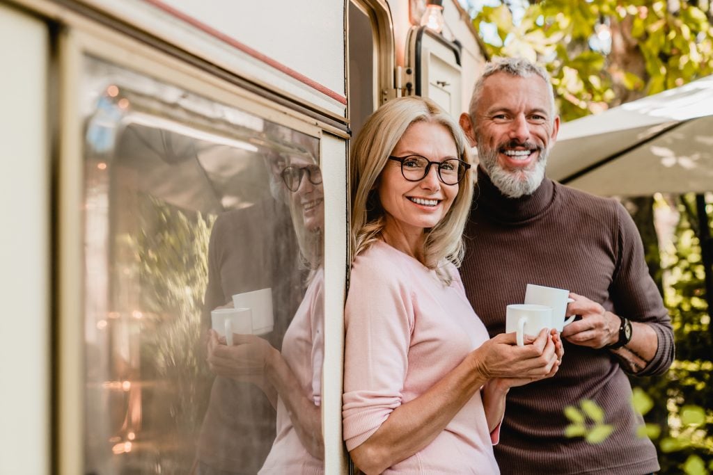 Older man and woman holding coffee mugs standing outside their RV, they are full-time RV living. 
