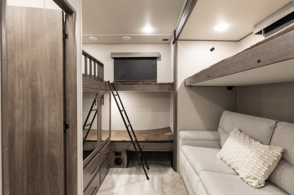 Interior shot of the bunk room of the Grand Design Solitude 3740BH fifth wheel. A white couch is on the right with a ladder on the left and the entrance door to the bathroom. This is one of the best RV for full time family living.