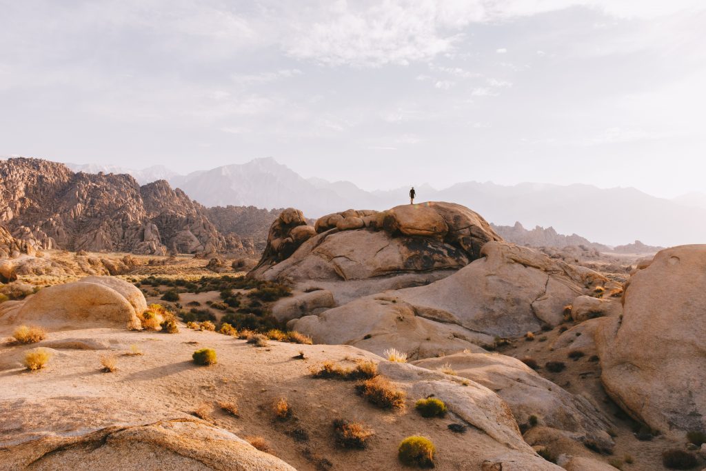 Person standing on a large rock overlooking a mountain range in the background. This was taken in Alabama Hills, a Boondocking location in California.