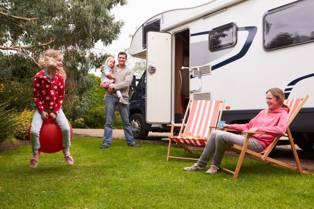 An rv living family sitting outside of their RV with a little girl bouncing on a ball. 