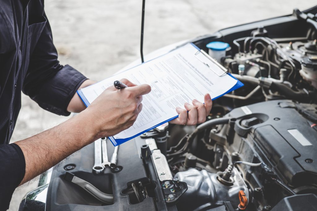 Man holding a checklist over an engine completing a PDI on a used RV. When you ask yourself if you should you buy a new or used RV, be sure to hire an inspector for used RVs.