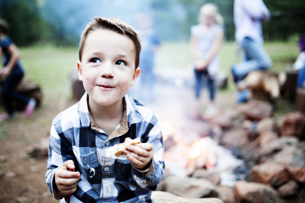 A little boy eating a smore with a campfire in the background. Family rv living includes many moments like this. 
