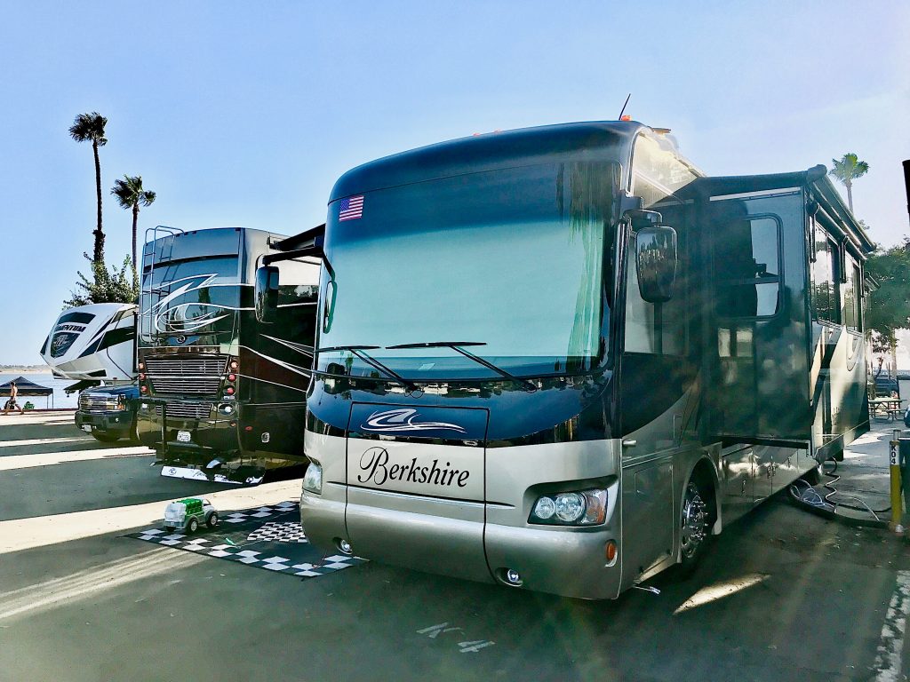 Class A Motorhome parked in an RV park with the ocean in the background. Depending on what RV parks you want to go to, you can ask yourself should you buy a new or used RV?