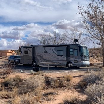 Motorhome parked at camp site in Wahweap campground amongst sand, trees and tumble weeds.