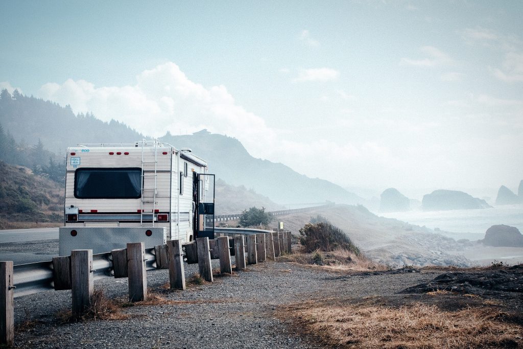 RV parked on the side of the road overlooking the ocean with some fog. Asking yourself if you should you buy a new or used RV will help determine where you travel. 