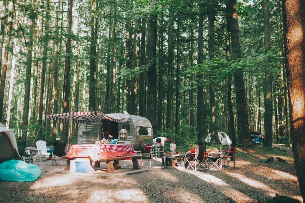 Vintage RV parked in tall trees with a picnic table and an rv living family outside playing. 