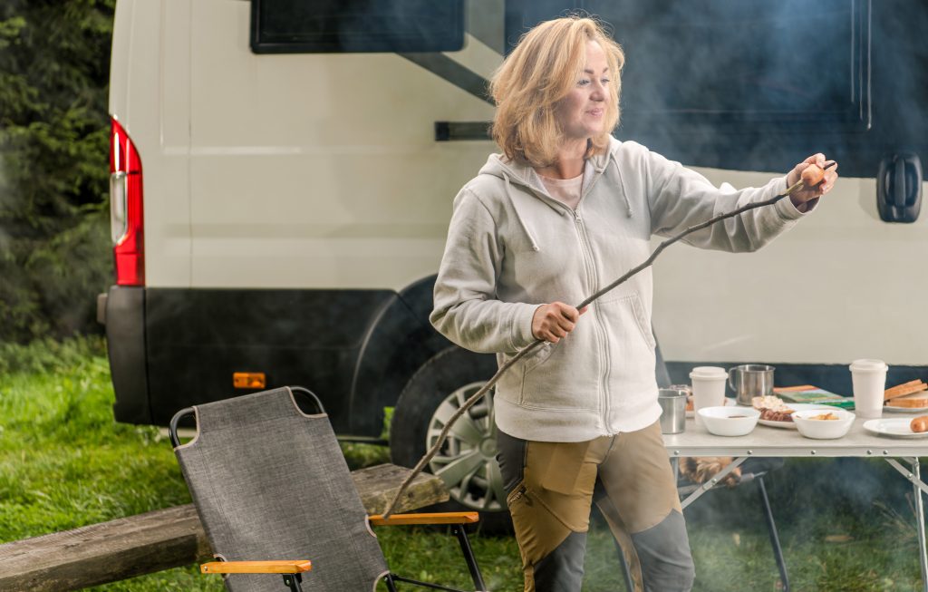 Woman standing in front of her Class B RV taking a roasted marshmallow off her stick. 