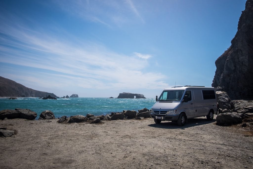 Class B RV parked on the sand with beautiful blue water in the background. 