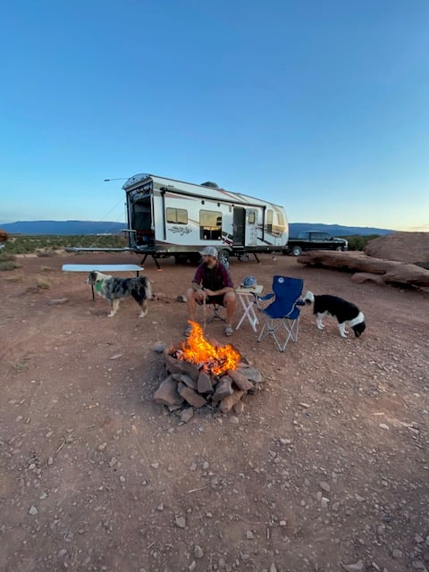 Man and 2 dogs beside fire in front of travel trailer