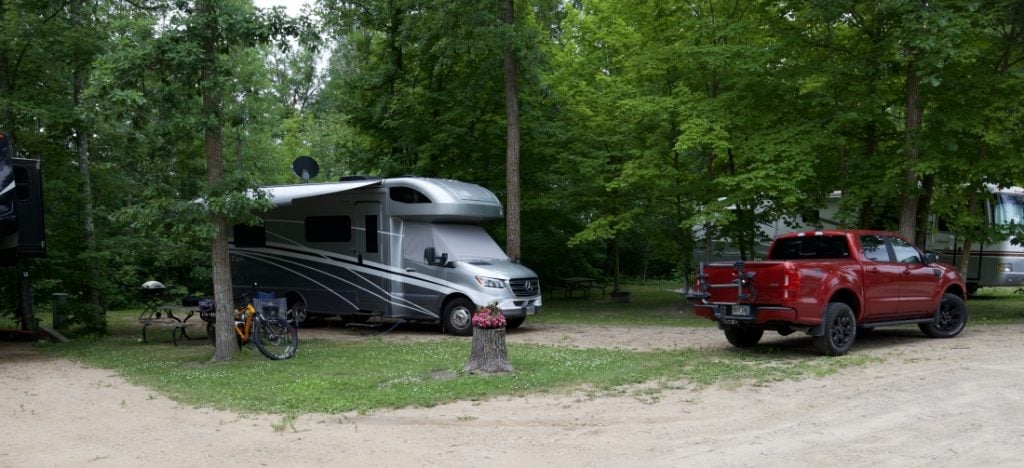 Gray Class C motorhome parked in an RV spot with red pickup and bicycles nearby - camping in Minnesota