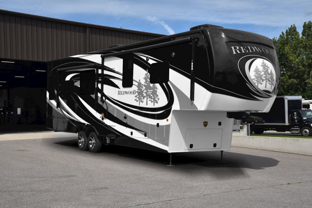 A large 5th wheel RV parked outside a garage