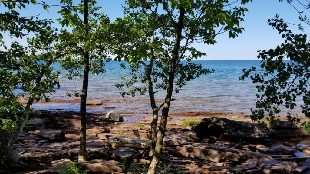 Trees in the foreground with Lake Superior in the background against a blue sky - view from RV parks in Michigan