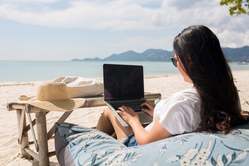 Woman sitting on the beach with her laptop. She's figured out how to get internet in an RV so she can work from anywhere. 