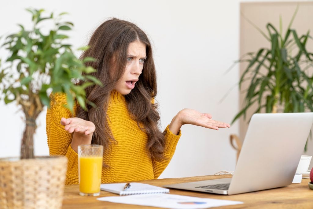 Woman with her hands up and looking frustrated at her laptop. how to get internet in an RV is an important question to answer so you don't face future headaches!