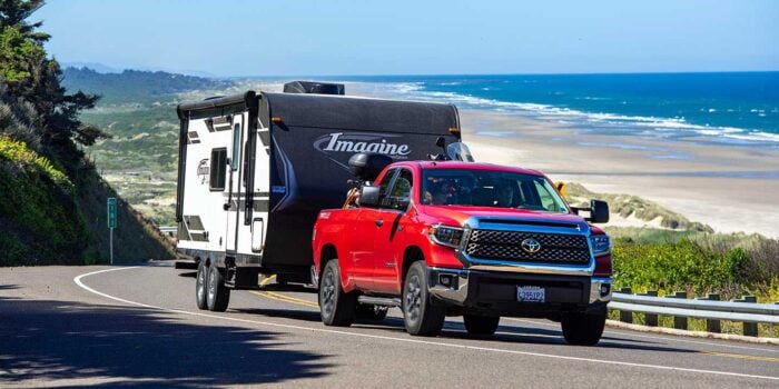 Red Toyota Tundra pickup truck towing a travel trailer near ocean