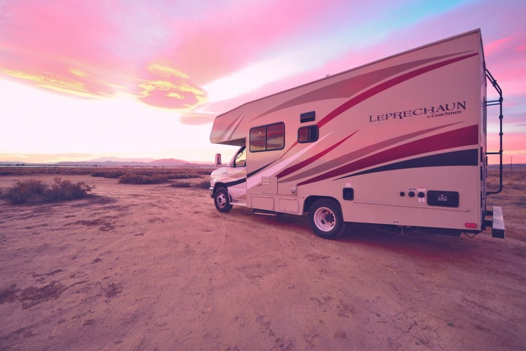 Class C RV parked in the dirt with a pretty sunset in the background