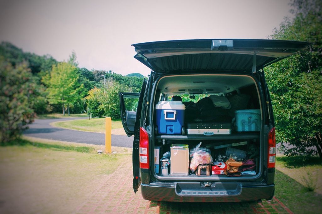 Back of a van with the trunk open and a bunch of luggage, coolers, and food piled in. 