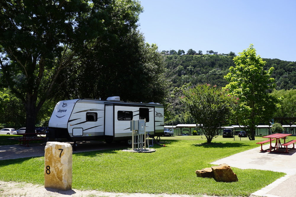White travel trailer in a site with trees in the background. Green grass in the foreground.