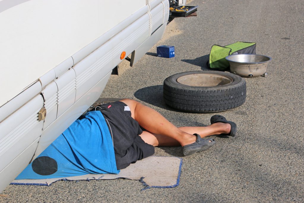 Man under RV repairing a tire of the RV he rented out 