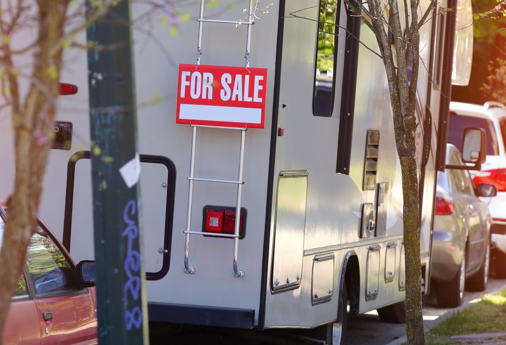 An RV parked on the street with a for sale sign on the back 