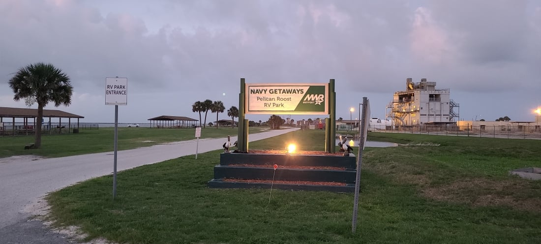 Welcome sign at Pelican Roost RV Park with palm trees and St Johns River in background.