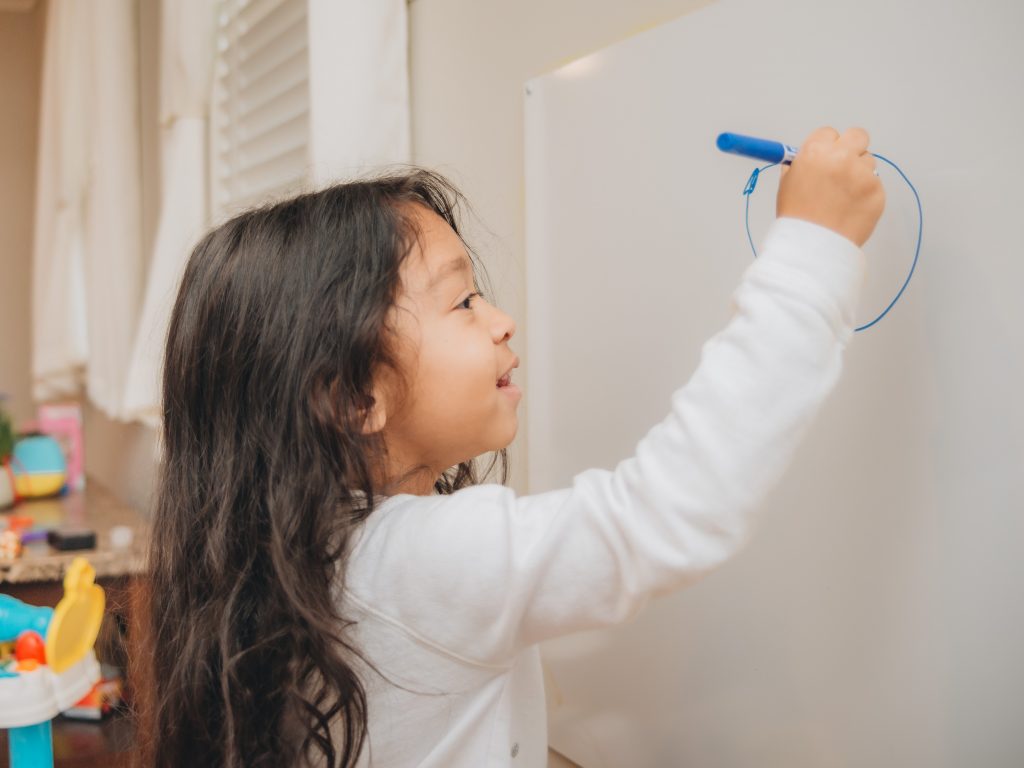 a little girl using the whiteboard and markers from her virtual school supply list