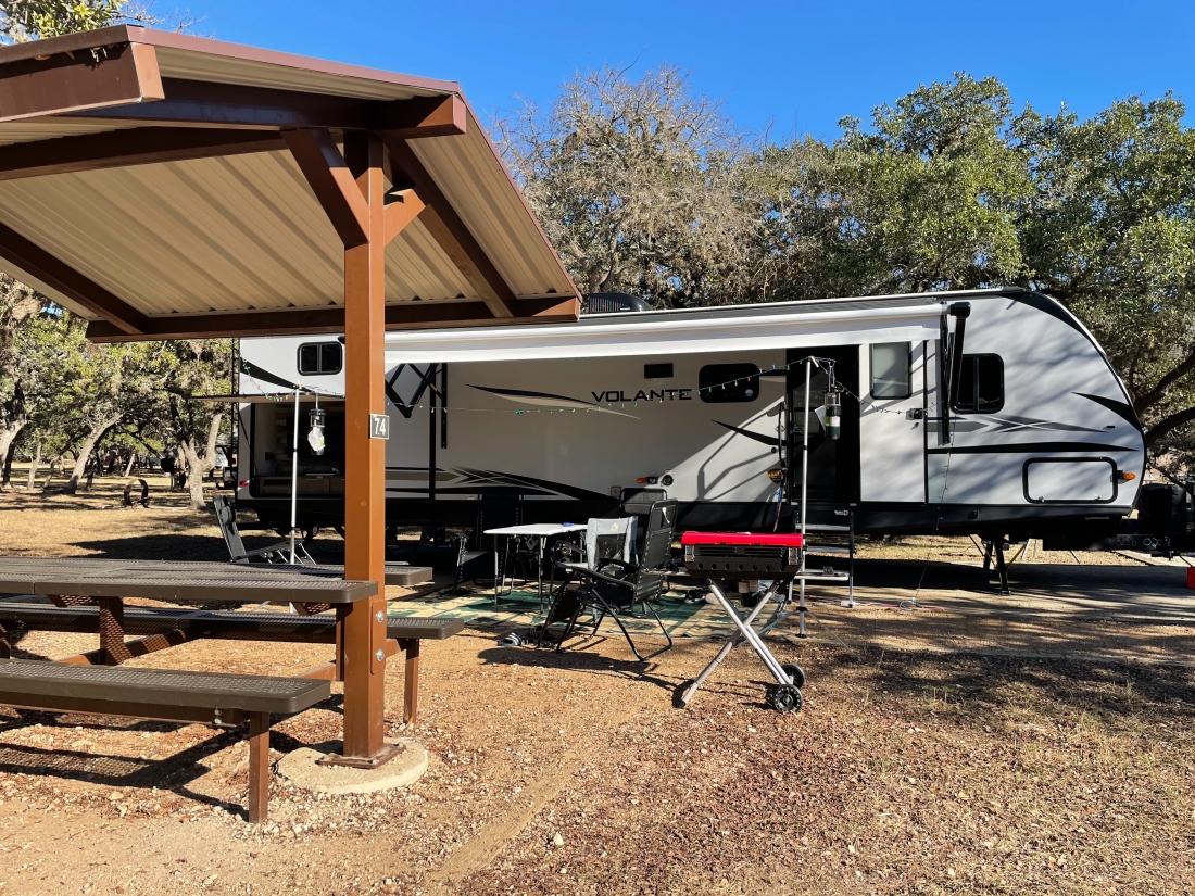 Covered picnic area beside travel trailer set up for camping