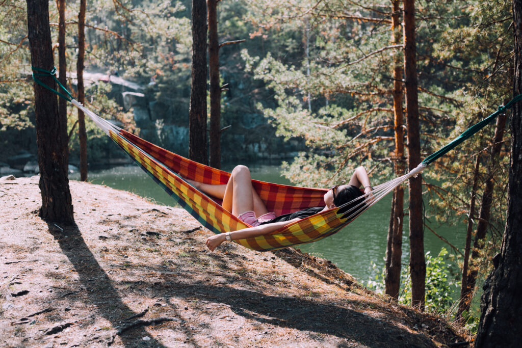 A woman in a hammock sleeping next to a body of water 