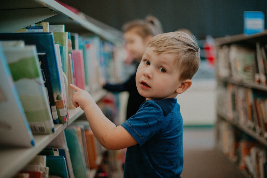 A little boy in a library looking at the different books, practicing unschooling, one of the different styles of homeschooling