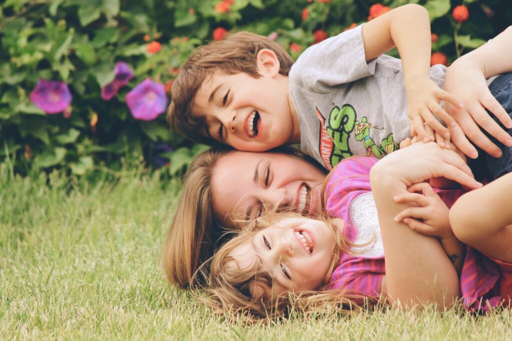a mom RV living with kids and laughing while rolling in the grass with her two children