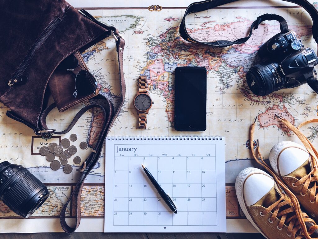 a map with a calendar, cell phone, shoes, bag, camera all sitting on top. It's important to travel plan with your children when RV living with kids