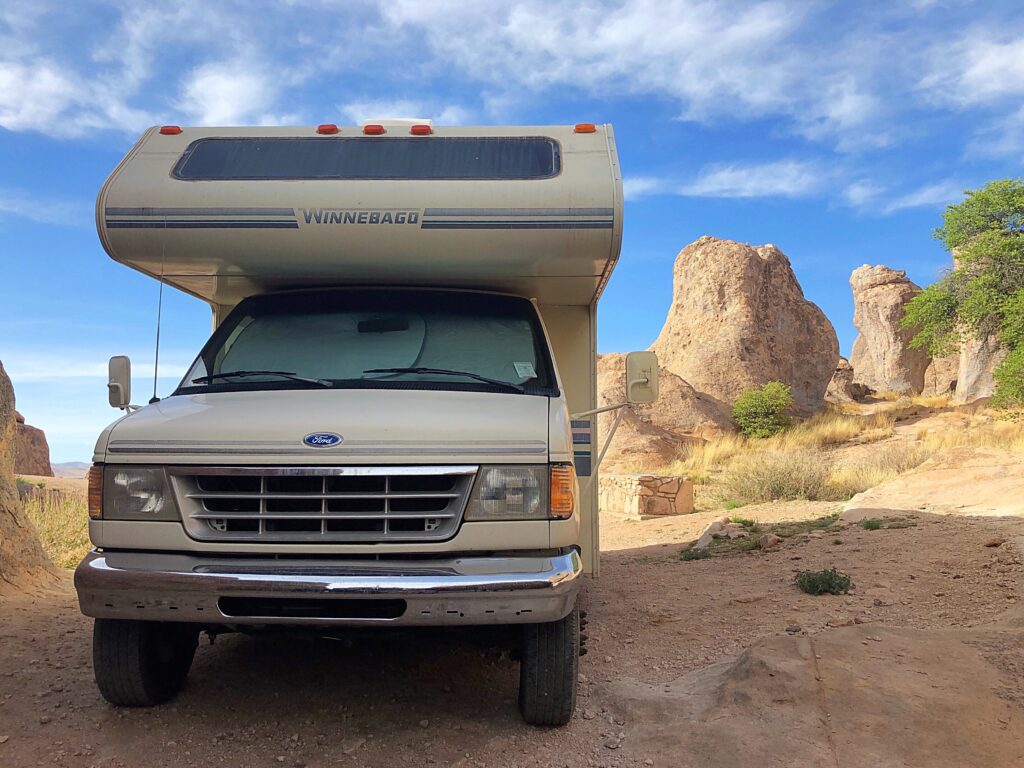 A Class C RV in the desert with rocks in the background 