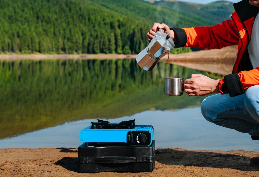 A person pouring coffee in front of a portable stove, an item they got off this Primitive Camping Checklist 