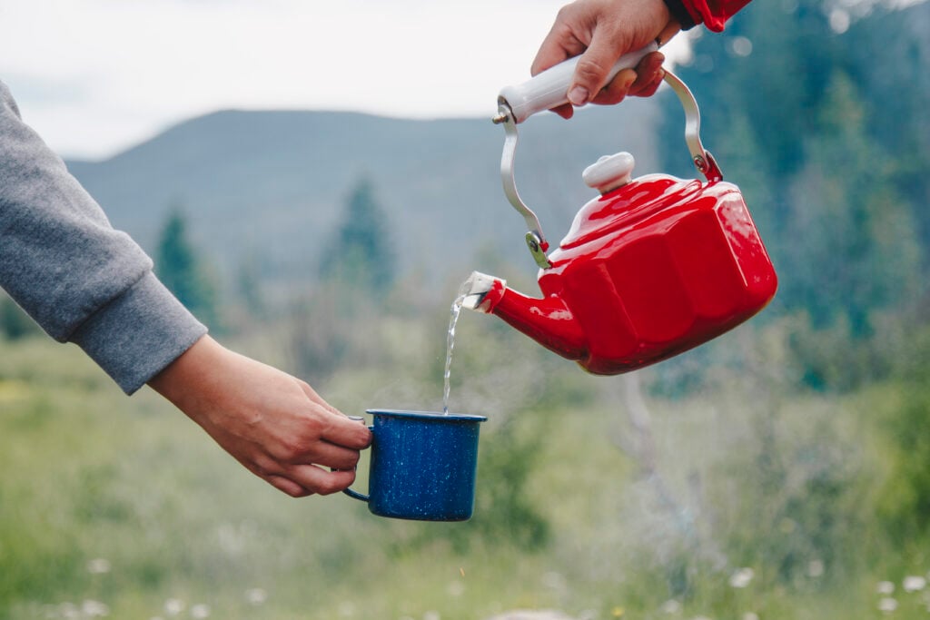 A tea kettle being poured into a mug. Clean drinking water is part of the Primitive Camping Checklist.