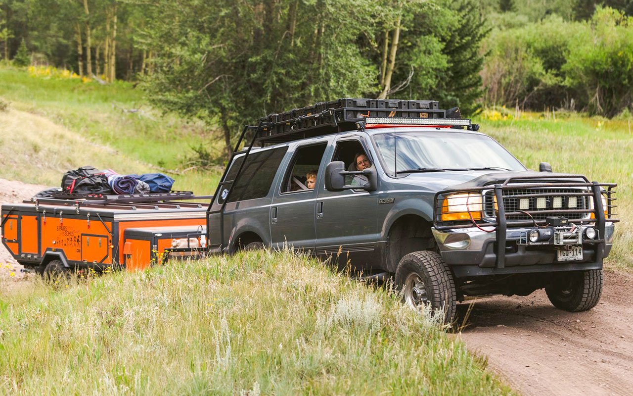 green SUV towing orange Opus folding camping trailer