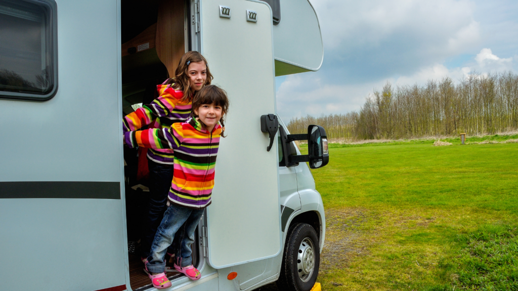 Two children leaning out of the door of an RV. 
