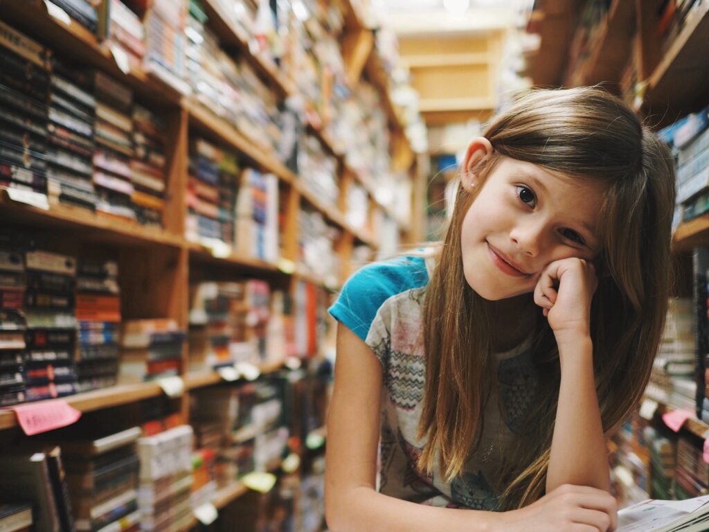 A young girl sitting in a library looking at the camera. It's important to know homeschool laws by state so you following the right guidelines