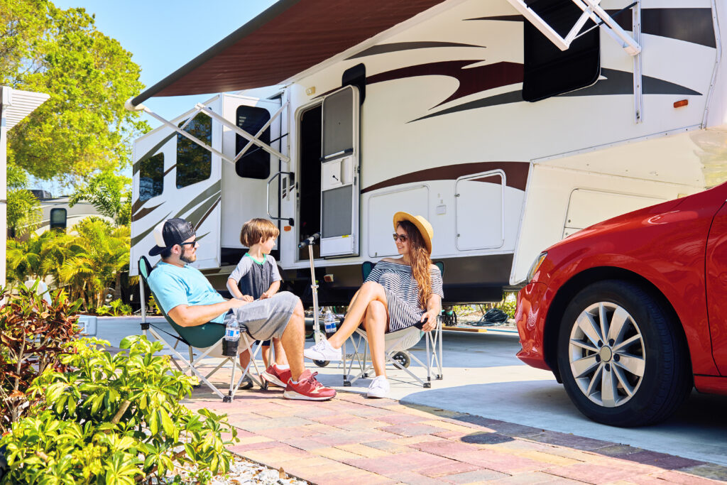 Family relaxes on patio campsite discussing their RV warranty outside their RV.