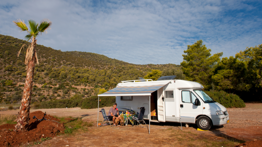 A man sitting outside his RV with mountains in the background. He has the best rv battery for boondocking so he can stay out longer.