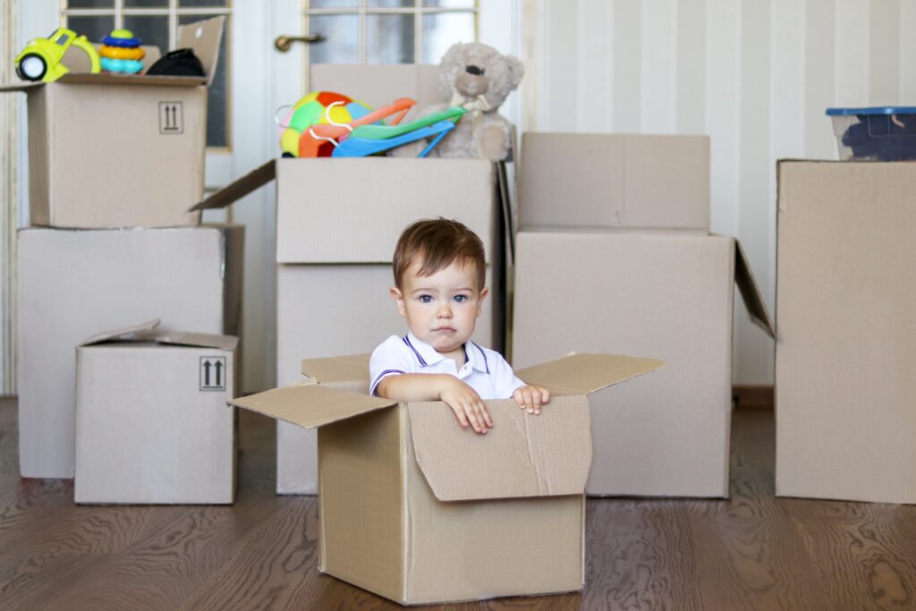 A baby boy sitting in a moving box with more boxed behind him. Part of learning how to travel full time with a family is downsizing. 